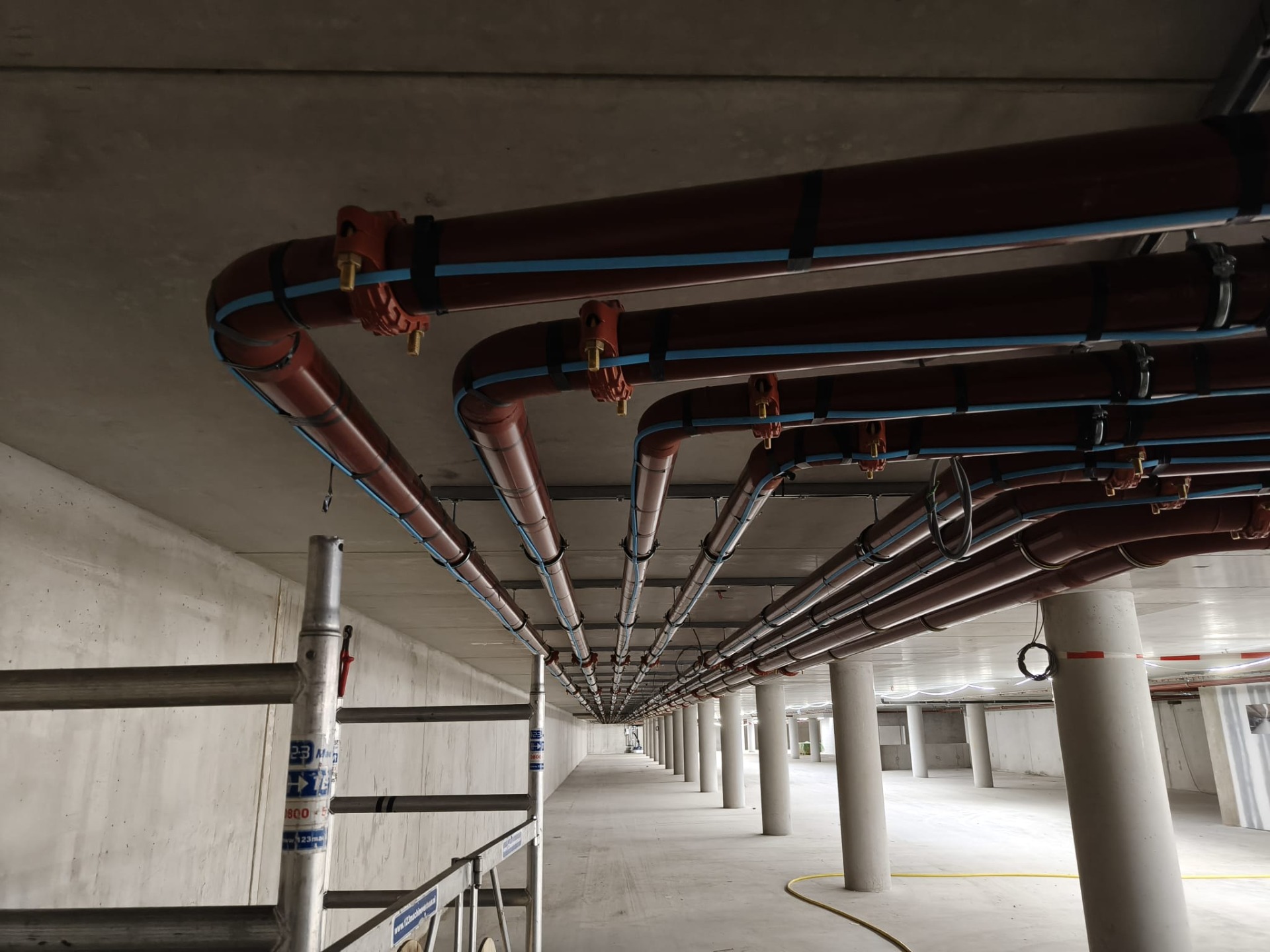 Rij stalen leidingen met blauwe tracing kabel aan het plafond in een lege keldergang.