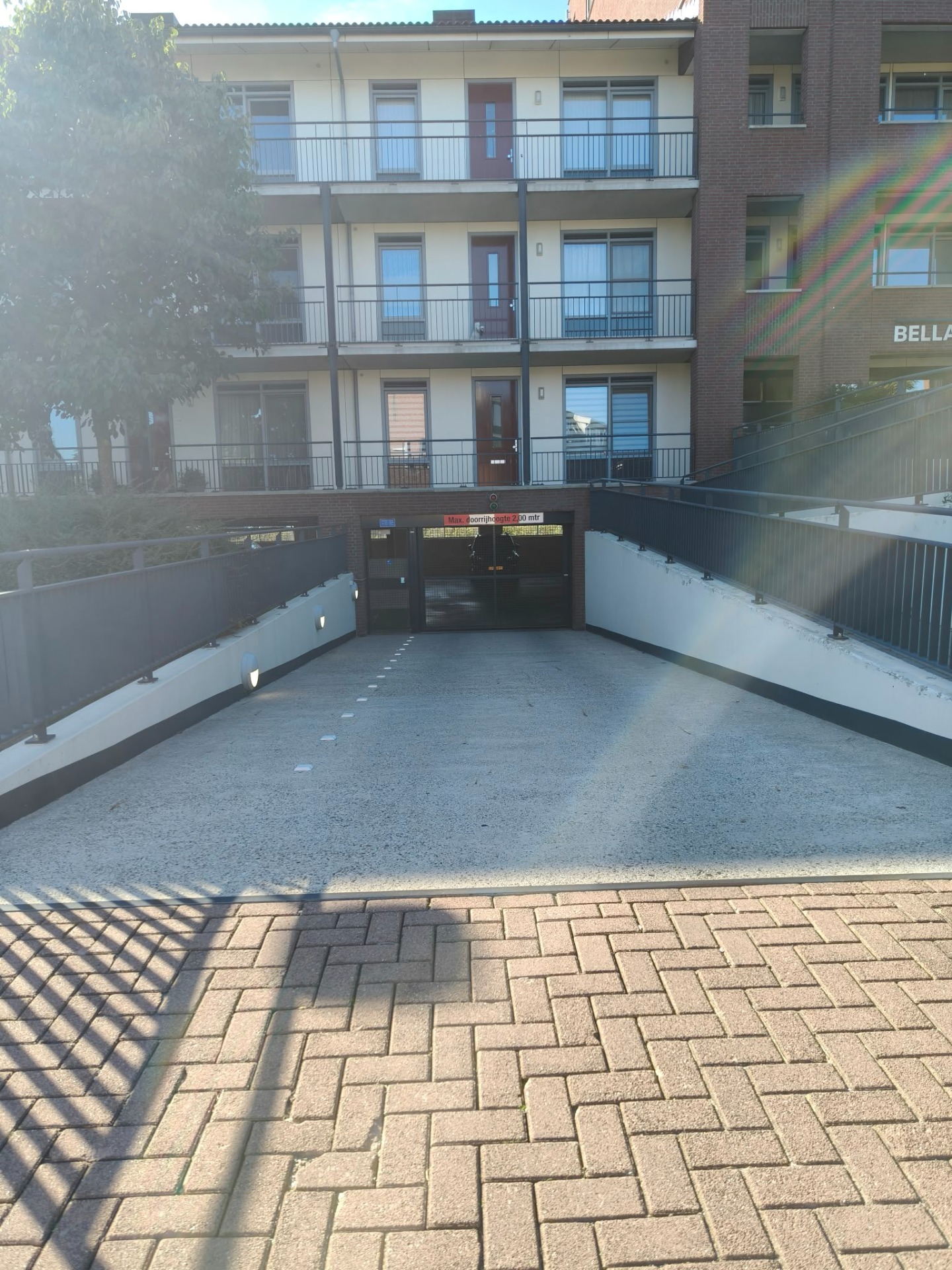 Binnenplaats met bakstenen appartementen, balkons met tralies, poort en regenboogreflectie in de lucht.